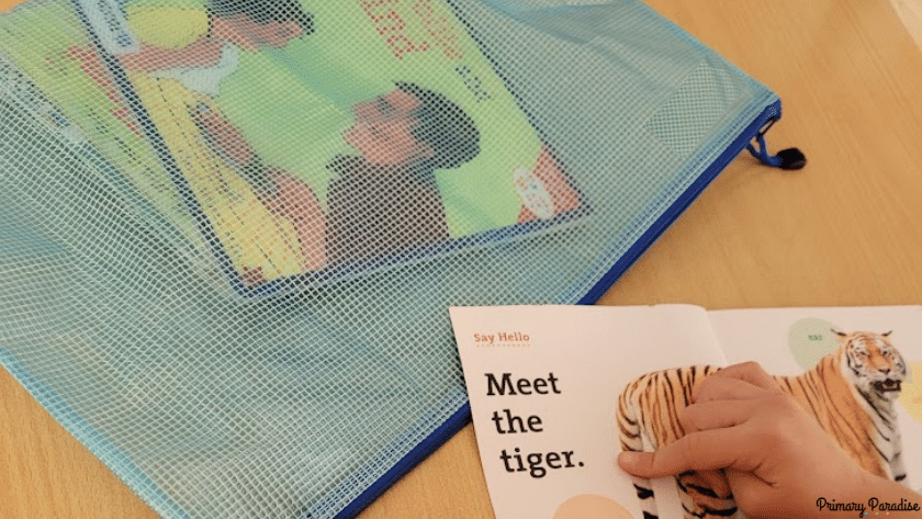An image of a plastic book bag with a zipper and the corner of a book with a child's finger pointing to the words.