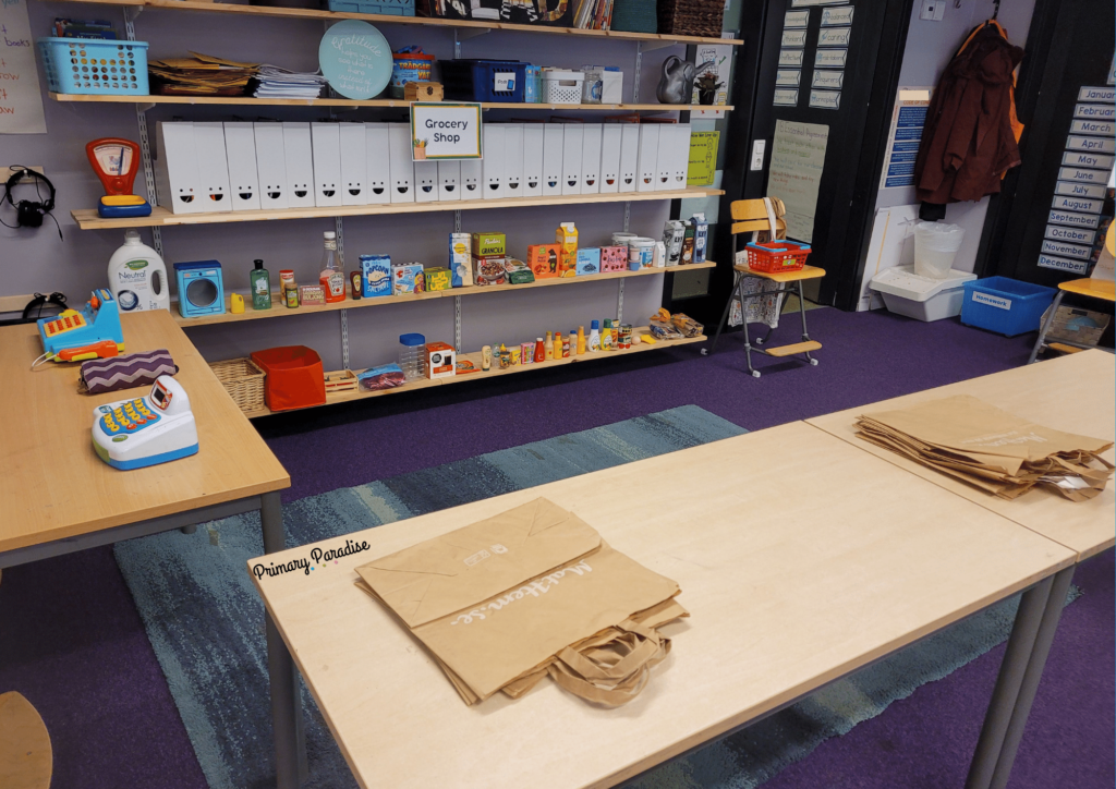 a grocery store center with food containers and play food lined up on a bookshelf, check out area, and bagging area