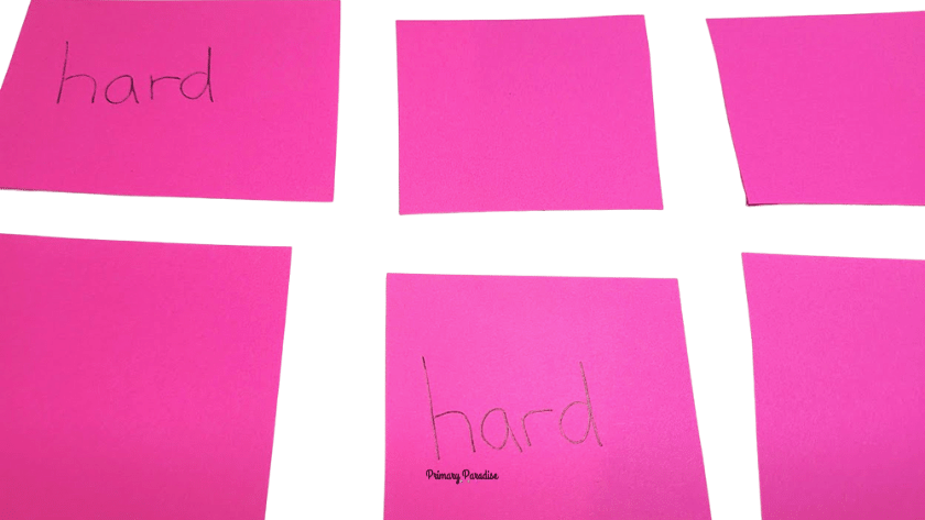 Squares of pink paper in a grid for a memory game. Two show the word hard on them.