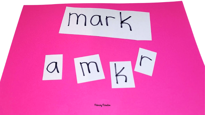 The word mark is written on a piece of white paper. Underneath, there are 4 squares of paper with the letters a, m, k, and r (to make the word mark).