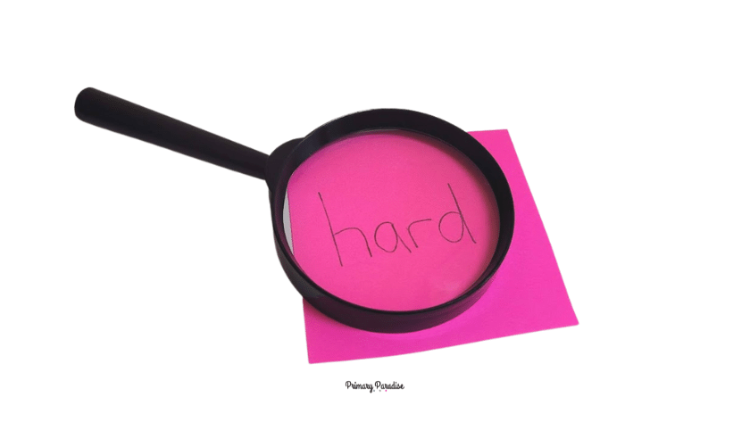 The word hard is written on a pink piece of paper. A magnifying glass is laying over the square.