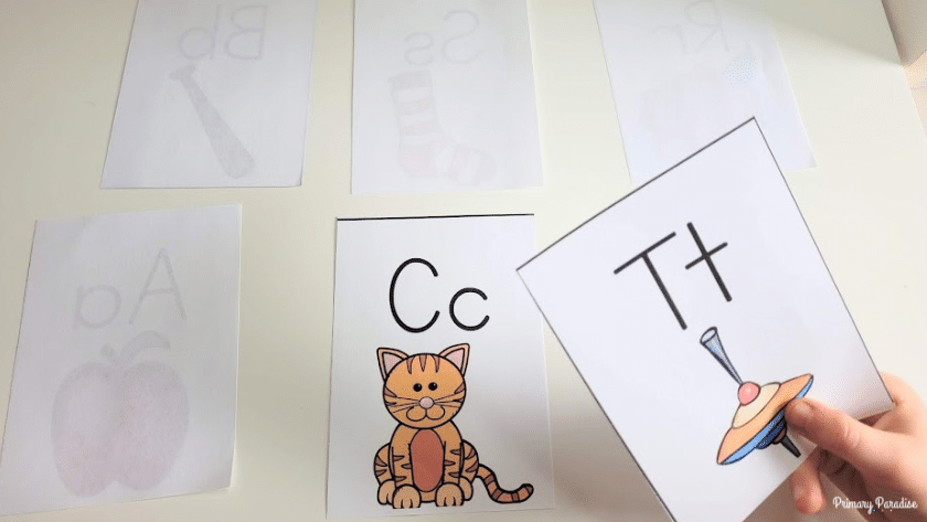 A picture of a child picking up a flashcard that says t. o the left is a flashcard with the letter c on it.