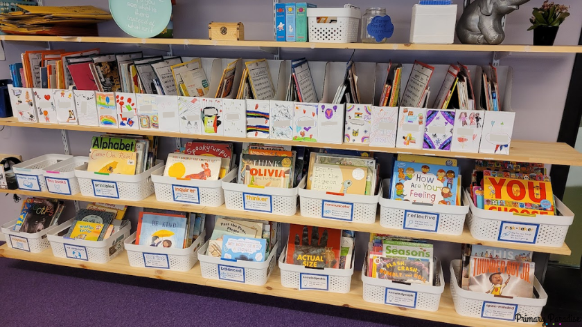 A picture of white bins with books on the. On each bin is a label with an IB learner profile characteristic and a definition of what it means.