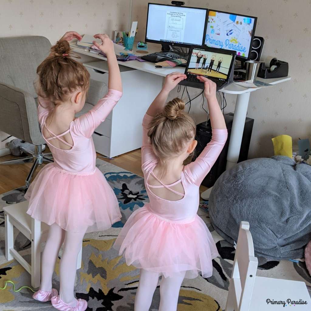 two girls in pink ballet outfits watching a ballet class on a tablet