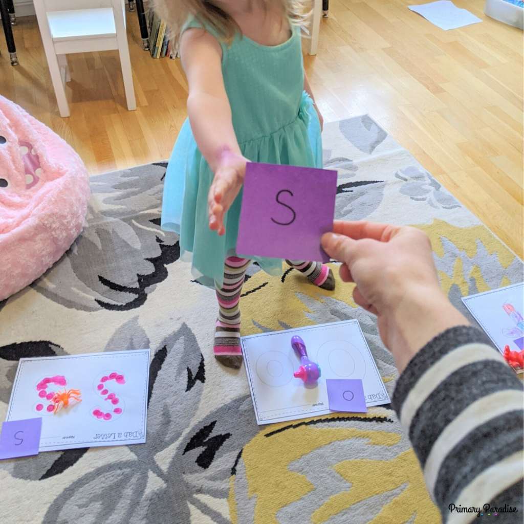 little girl taking a sticky note with the letter s on it. She's sorting letters on sticky notes to match with posters with the same letters